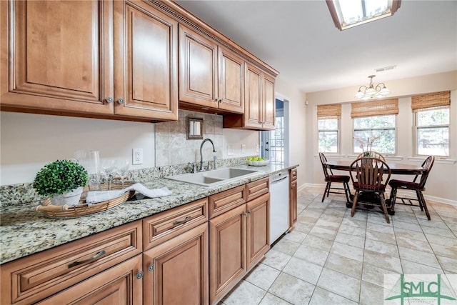 kitchen featuring light stone counters, white dishwasher, sink, decorative light fixtures, and a chandelier