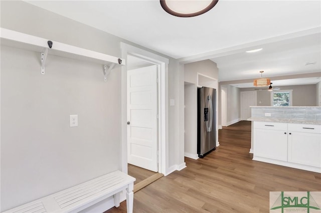 interior space featuring pendant lighting, stainless steel refrigerator with ice dispenser, ceiling fan, light stone counters, and white cabinetry