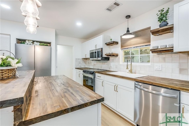 kitchen with appliances with stainless steel finishes, decorative light fixtures, white cabinetry, and butcher block counters