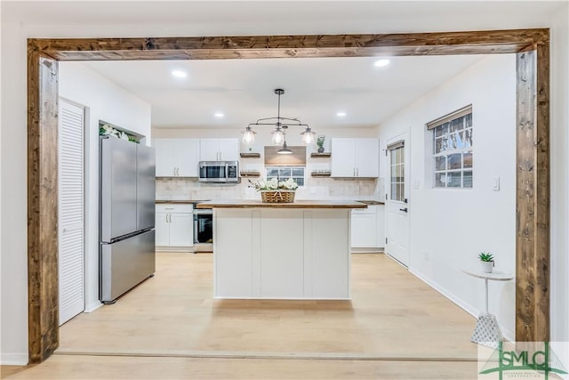 kitchen featuring white cabinets, appliances with stainless steel finishes, a kitchen island, and hanging light fixtures