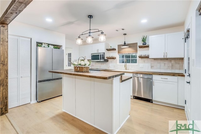 kitchen with white cabinets, a center island, stainless steel appliances, and butcher block counters