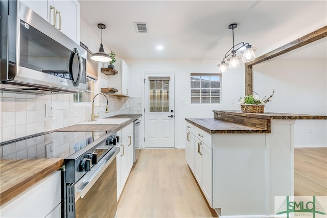 kitchen featuring wooden counters, appliances with stainless steel finishes, sink, white cabinetry, and hanging light fixtures