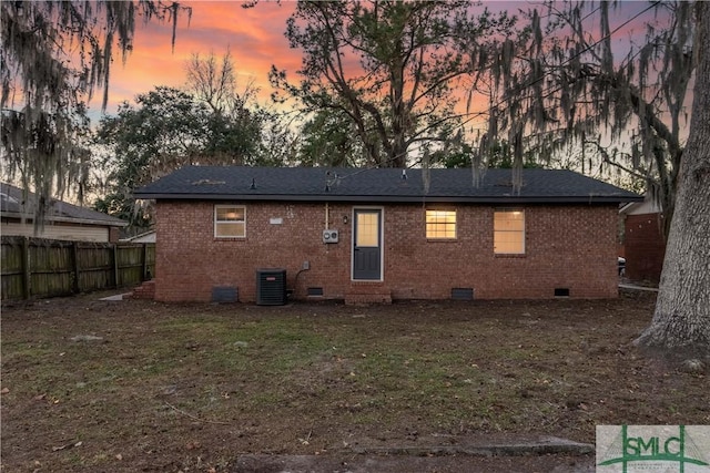 back house at dusk with a yard and central AC unit