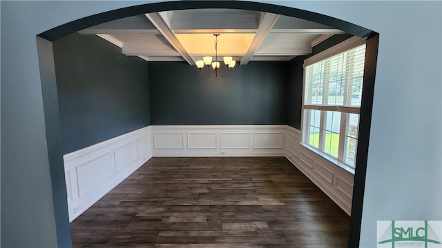 unfurnished dining area with dark wood-type flooring, coffered ceiling, beamed ceiling, a notable chandelier, and ornamental molding