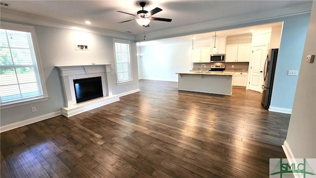 unfurnished living room with ceiling fan, sink, dark wood-type flooring, a brick fireplace, and crown molding