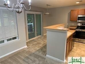 kitchen with an inviting chandelier, pendant lighting, light colored carpet, a kitchen island, and appliances with stainless steel finishes