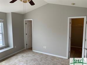 unfurnished bedroom featuring light carpet, ceiling fan, a spacious closet, a closet, and lofted ceiling