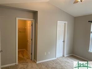 unfurnished bedroom with lofted ceiling, light carpet, a walk in closet, ceiling fan, and a closet