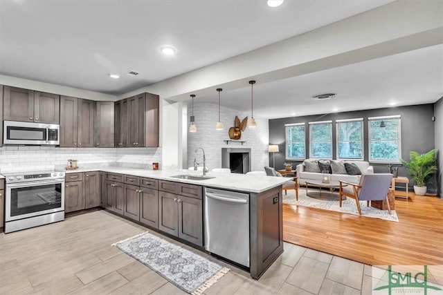 kitchen with kitchen peninsula, decorative backsplash, stainless steel appliances, sink, and pendant lighting