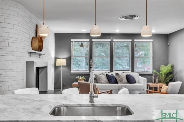 kitchen featuring a fireplace, light stone countertops, sink, and hanging light fixtures