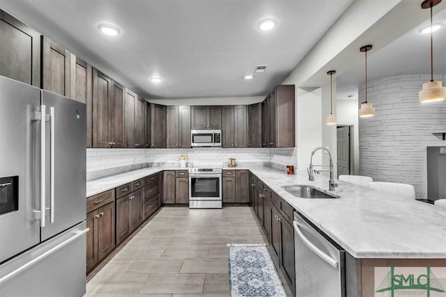 kitchen featuring appliances with stainless steel finishes, tasteful backsplash, light stone counters, sink, and hanging light fixtures