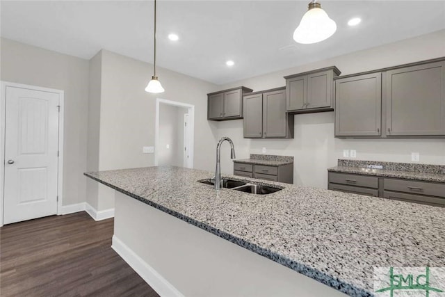 kitchen with sink, dark wood-type flooring, light stone counters, pendant lighting, and gray cabinets