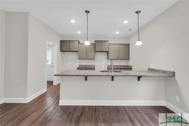 kitchen with a kitchen bar, sink, hanging light fixtures, light stone counters, and kitchen peninsula