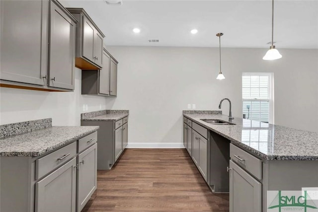 kitchen featuring sink, dark wood-type flooring, light stone counters, kitchen peninsula, and pendant lighting