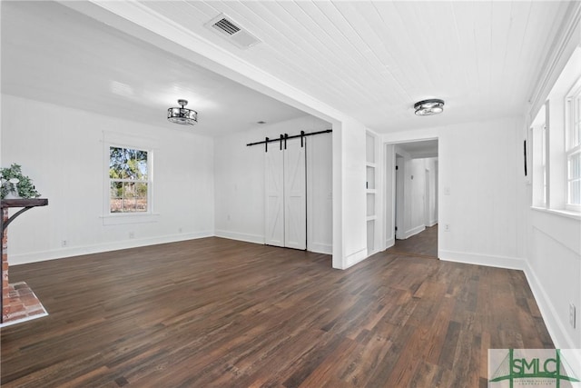 unfurnished living room featuring a barn door, built in shelves, and dark wood-type flooring