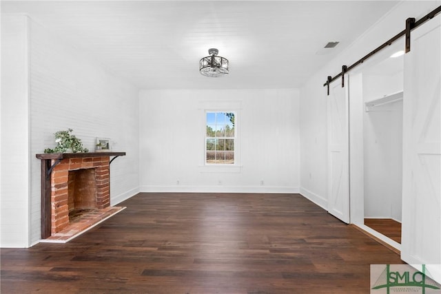 unfurnished living room featuring a barn door, dark wood-type flooring, and a brick fireplace