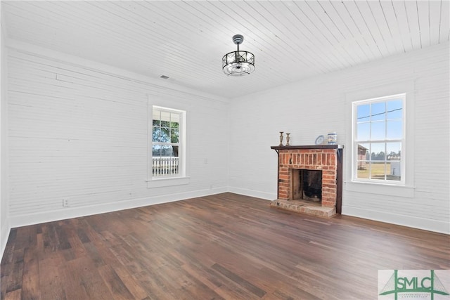 unfurnished living room with an inviting chandelier, dark hardwood / wood-style flooring, a wealth of natural light, and a brick fireplace