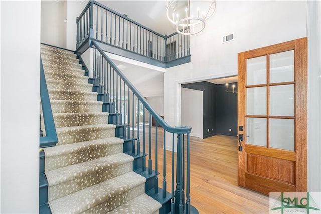 stairs featuring hardwood / wood-style floors, a towering ceiling, and an inviting chandelier