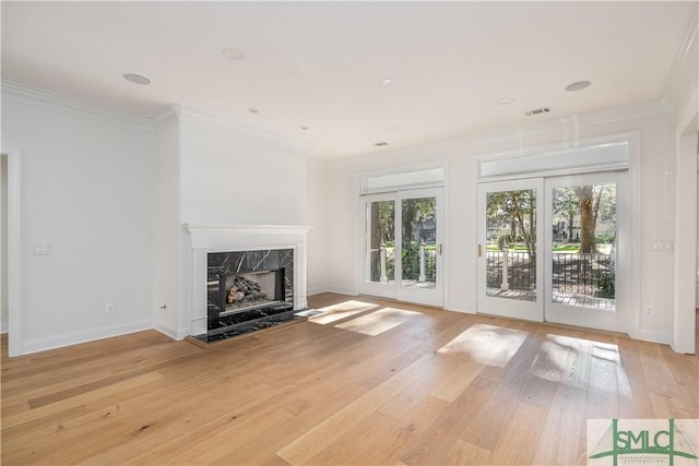 unfurnished living room featuring a high end fireplace, french doors, light wood-type flooring, and ornamental molding