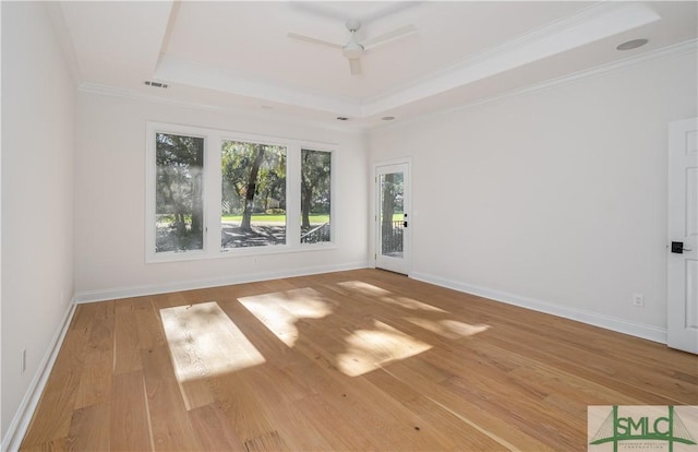 empty room featuring ceiling fan, light wood-type flooring, ornamental molding, and a tray ceiling