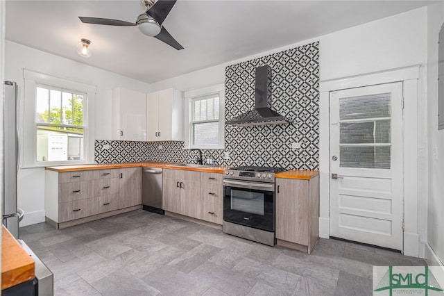 kitchen with wooden counters, appliances with stainless steel finishes, ventilation hood, ceiling fan, and sink