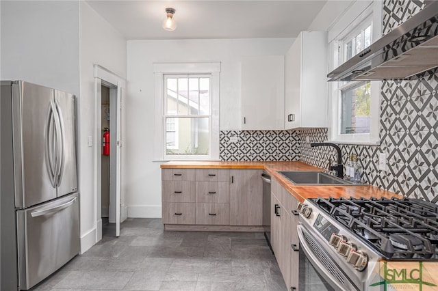 kitchen with sink, stainless steel appliances, wall chimney range hood, butcher block countertops, and decorative backsplash