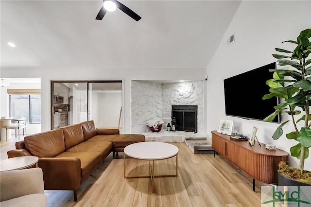 living room featuring ceiling fan, vaulted ceiling, a fireplace, and light hardwood / wood-style flooring