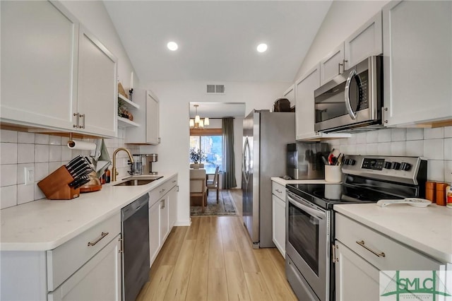 kitchen with white cabinets, sink, vaulted ceiling, light hardwood / wood-style floors, and stainless steel appliances