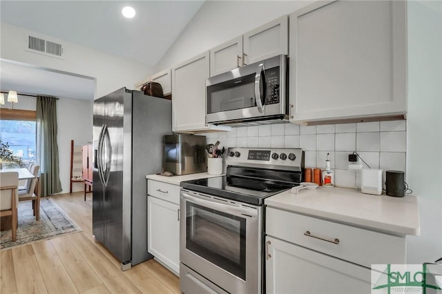 kitchen featuring stainless steel appliances, tasteful backsplash, light hardwood / wood-style flooring, lofted ceiling, and white cabinets