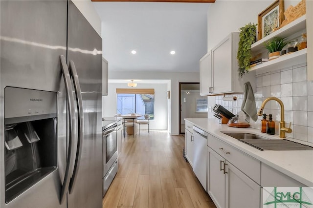 kitchen featuring white cabinets, sink, light hardwood / wood-style flooring, decorative backsplash, and appliances with stainless steel finishes