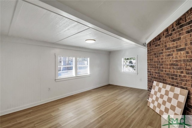 spare room featuring light hardwood / wood-style floors and brick wall