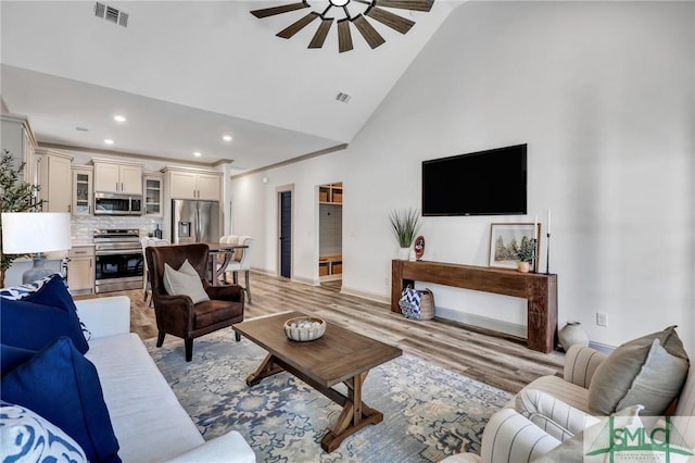 living room with ceiling fan, high vaulted ceiling, and light hardwood / wood-style flooring