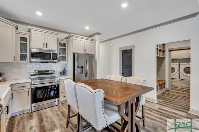 kitchen with washing machine and clothes dryer, tasteful backsplash, light wood-type flooring, appliances with stainless steel finishes, and ornamental molding