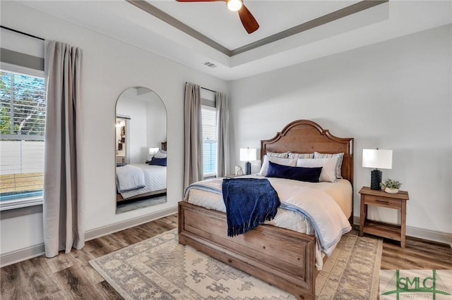 bedroom with a tray ceiling, ceiling fan, and wood-type flooring