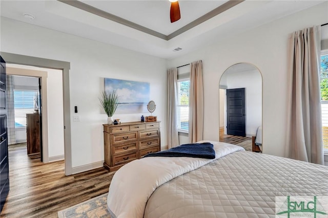 bedroom with wood-type flooring, a raised ceiling, and ceiling fan