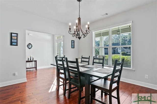 dining area featuring a healthy amount of sunlight, dark hardwood / wood-style flooring, and an inviting chandelier