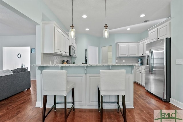 kitchen with decorative backsplash, appliances with stainless steel finishes, white cabinetry, and a kitchen breakfast bar