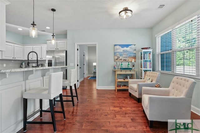 kitchen featuring tasteful backsplash, light stone counters, a breakfast bar, stainless steel fridge with ice dispenser, and white cabinetry