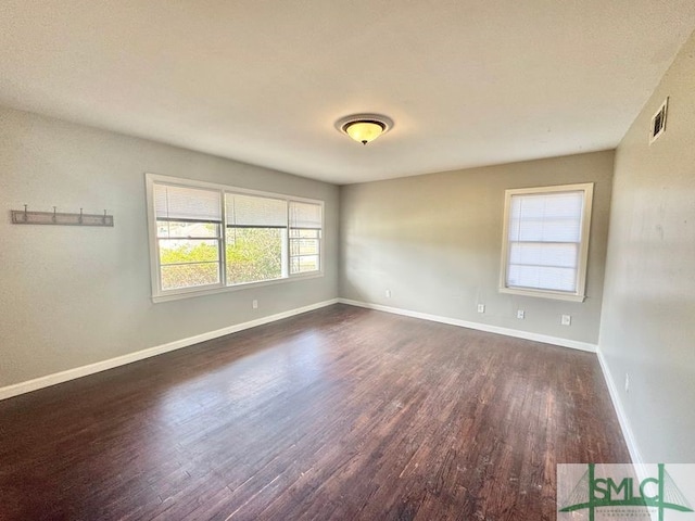 unfurnished room with visible vents, baseboards, and dark wood-style flooring