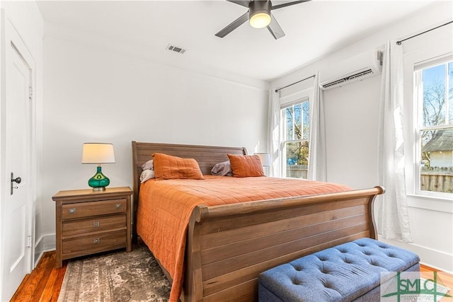 bedroom with a wall mounted air conditioner, dark hardwood / wood-style flooring, and ceiling fan