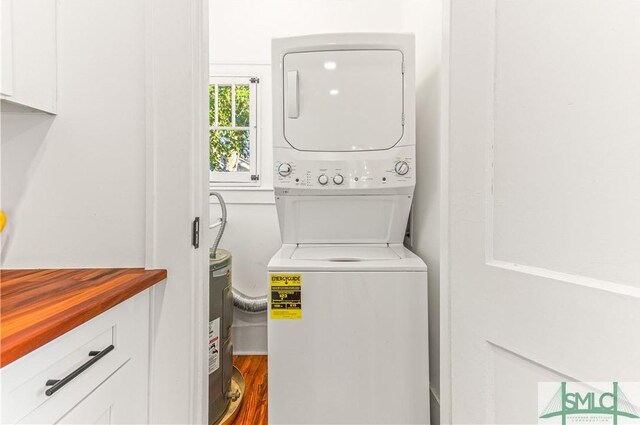 laundry area featuring electric water heater, cabinets, wood-type flooring, and stacked washer / dryer