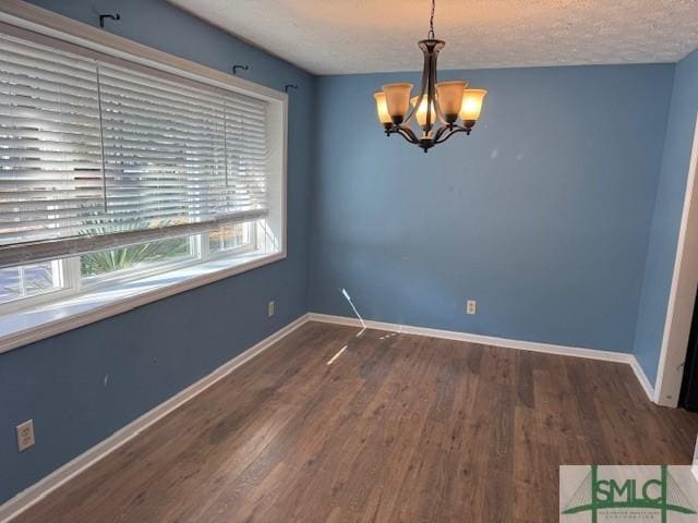 empty room with dark hardwood / wood-style flooring, a textured ceiling, and an inviting chandelier