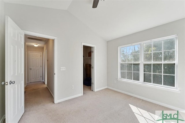 unfurnished bedroom featuring ceiling fan, light colored carpet, vaulted ceiling, a walk in closet, and a closet