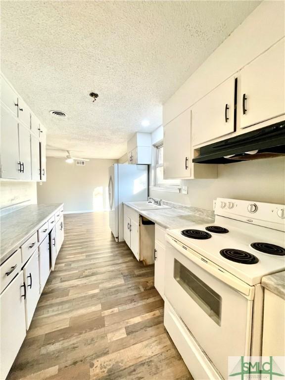 kitchen with white cabinetry, sink, light hardwood / wood-style floors, a textured ceiling, and white appliances