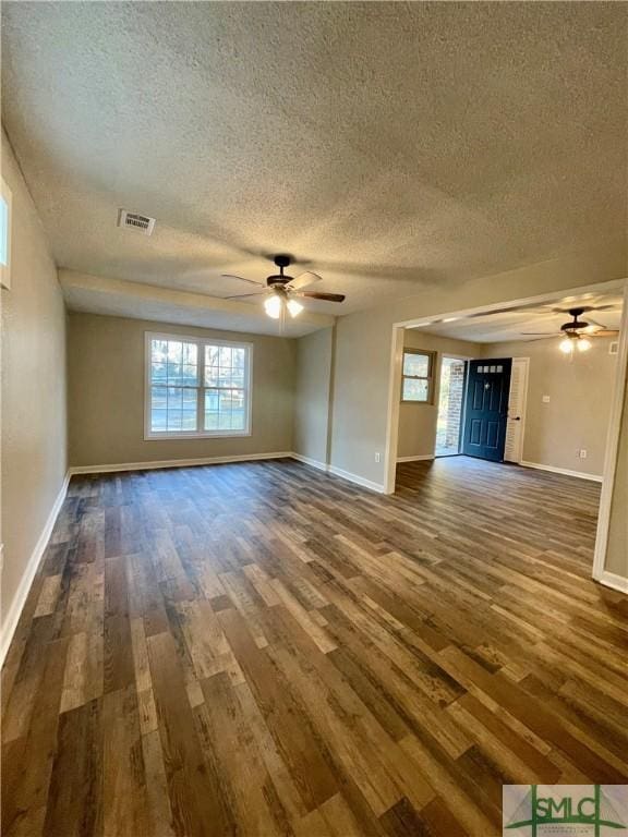 unfurnished living room featuring a textured ceiling, ceiling fan, a healthy amount of sunlight, and dark wood-type flooring