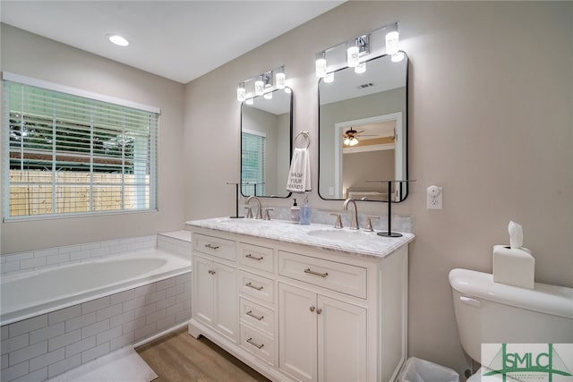 bathroom featuring vanity, tiled bath, toilet, and ceiling fan