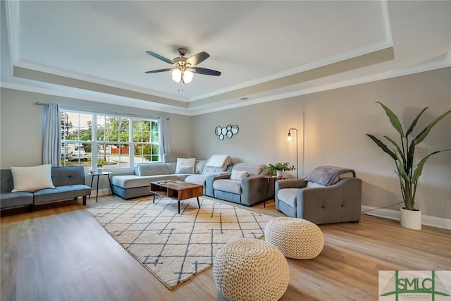 living room with ceiling fan, light hardwood / wood-style floors, a raised ceiling, and ornamental molding