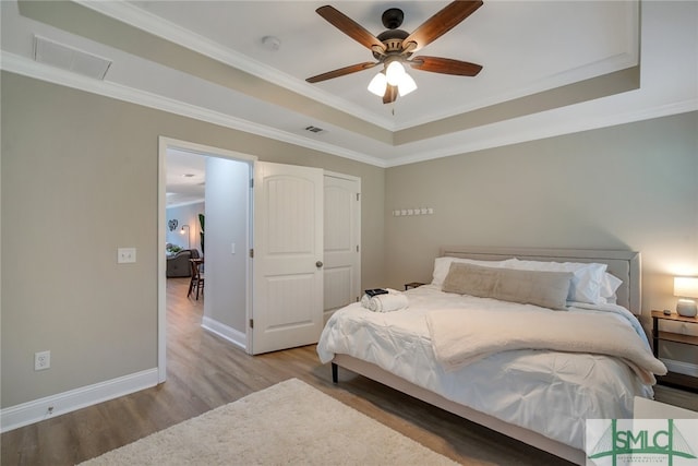 bedroom featuring a tray ceiling, crown molding, ceiling fan, and light hardwood / wood-style floors