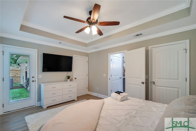 bedroom featuring ceiling fan, light wood-type flooring, access to outside, and a tray ceiling