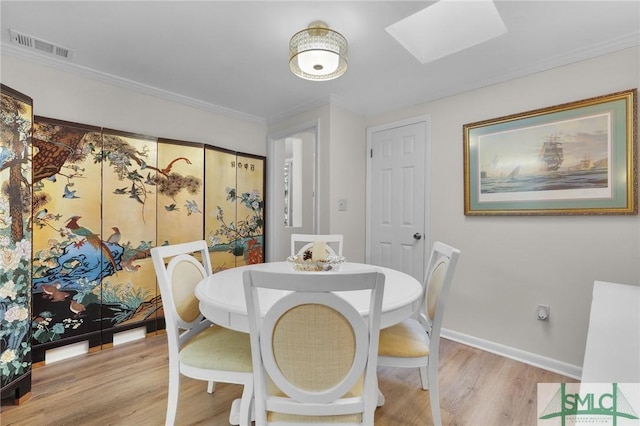 dining space with light hardwood / wood-style floors, crown molding, and a skylight